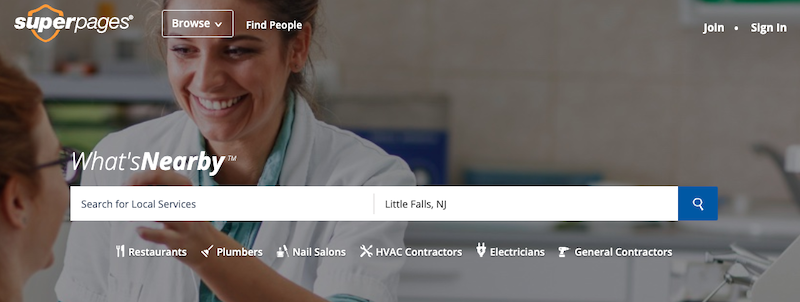 A smiling woman assisting another person in a bright room, with a search bar for local services overlaid on the image. The options include Restaurants, Plumbers, Nail Salons, HVAC Contractors, Electricians, and General Contractors.