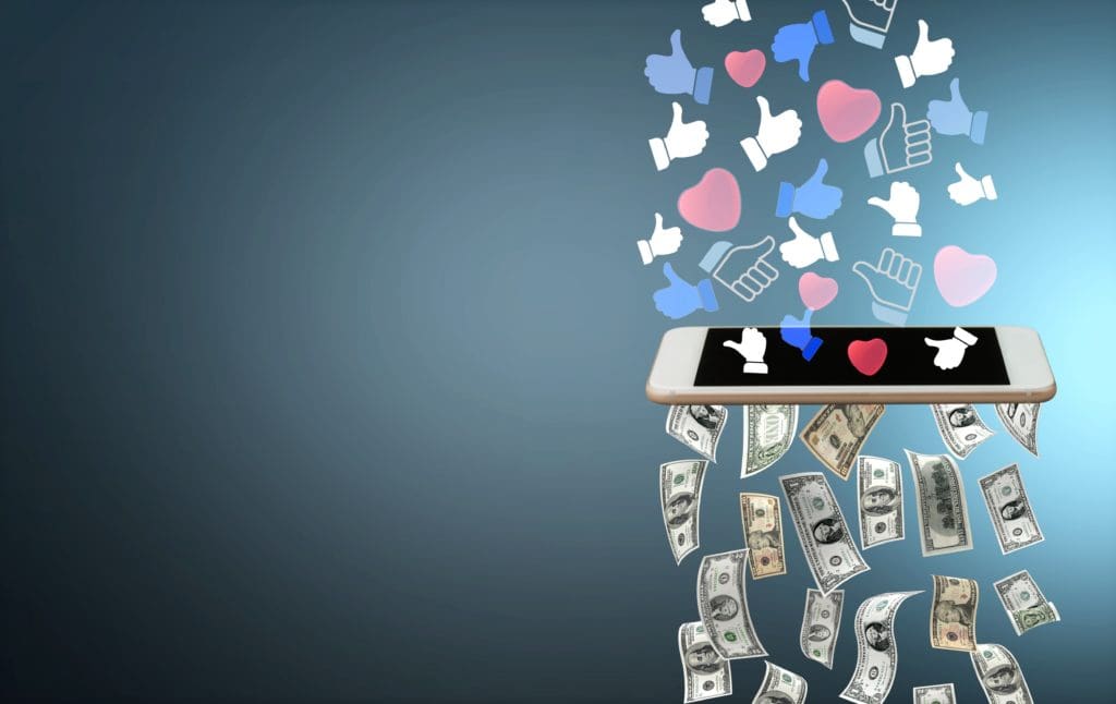 A smartphone screen displays floating icons of thumbs-up and hearts, symbolizing likes on social media. Below the phone, U.S. dollar bills cascade down, highlighting the vital role of social media in business and its connection to financial success. The background is a gradient blue.