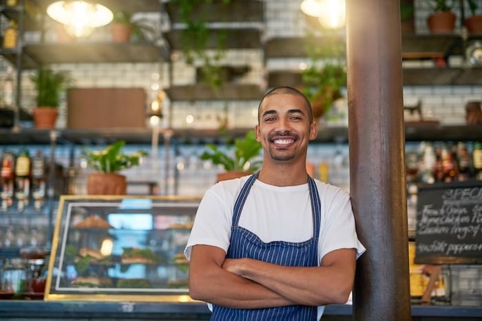 A smiling man in an apron standing in front of a restaurant, representing reputation management consultants.