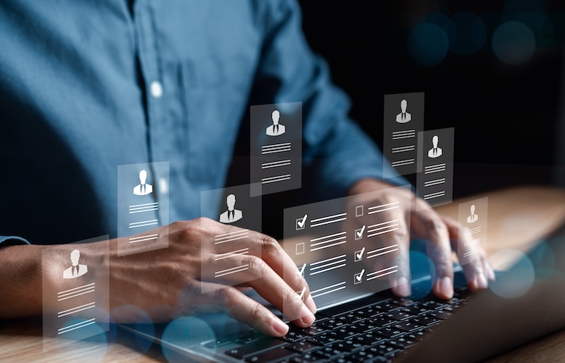 A person typing on a laptop with floating digital icons representing profiles and checklists. The image conveys a concept of online data management or digital networking.