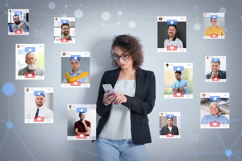 A woman with curly hair and glasses stands using a smartphone. Around her are profile cards of diverse men, each with heart and message icons, set against a digital network background. She's mindful of how to protect your privacy online while navigating the virtual dating world.