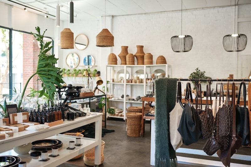 A cozy boutique interior with a minimalist design, this space showcases various home decor items including woven baskets, vases, hanging lamps, and bags. Shelves display bottles and other small products, while large green plants add a natural touch—perfectly captured on our Google Business Panel.