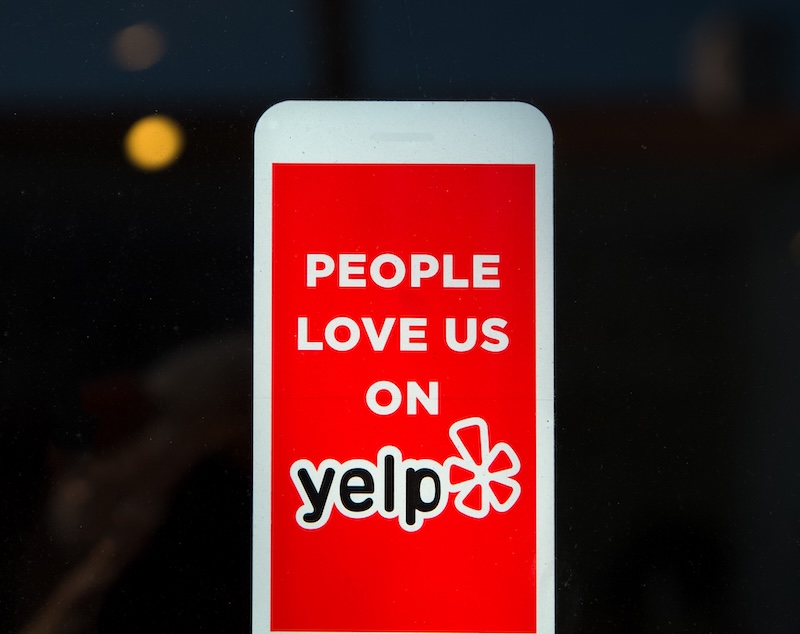 A red sign with white text declares, "People love us on Yelp," proudly highlighting the Yelp logo with its signature starburst, testament to our stellar business reviews.