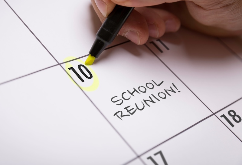 A calendar with the date "10" highlighted in yellow, marked with the words "School Reunion!" A hand is holding a pen, presumably having just circled this important date. If you'd rather stay home and binge your favorite shows, it's tough to opt out of a school reunion that promises so many memories.