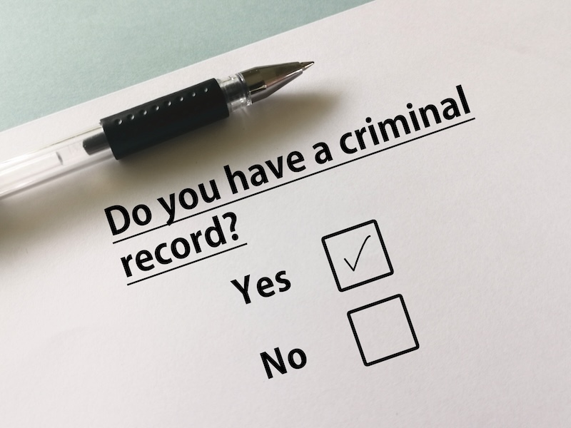 A form asks, "Do you have a criminal record?" with the "Yes" option ticked. A pen rests at the top left corner of the paper, hinting at the next steps for those pondering how to clear your record of a felony.