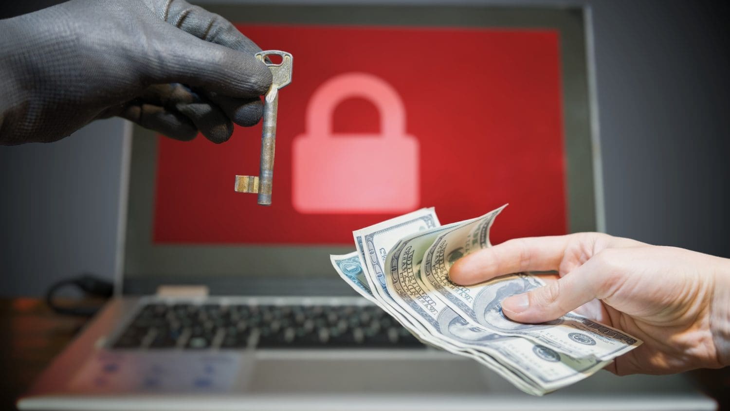 A gloved hand holds a key as another offers cash in front of a laptop displaying a red screen with a lock icon, vividly illustrating an online extortion scenario.