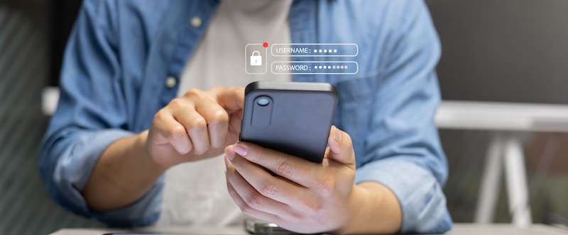 A person in a blue shirt holds a smartphone, cautiously inputting login credentials. A digital overlay shows username, password fields, and a padlock icon, symbolizing a secure defense against online extortion attempts.