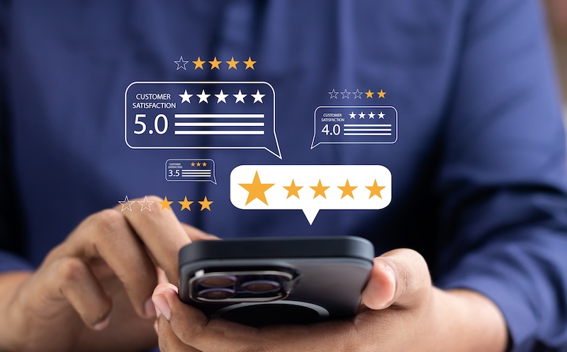 A person holds a smartphone, showcasing digital review bubbles with ratings of 4.0, 3.5, and 5.0 stars above the screen. The blurred background emphasizes the focus on mobile reviews and feedback, highlighting the importance of effective online presence management.