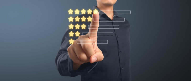 A person in a black shirt points to a virtual screen displaying a five-star rating system, engaging with the interface. This interaction hints at online presence management strategies. The background is dark gray, emphasizing the digital focus.