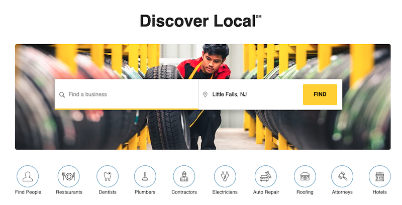 A young person in a warehouse examines a tire. Above is the text "Discover Local" and a search bar with "Find a business" and "Little Falls, NJ" filled in. Below, various round icons represent categories like restaurants, dentists, and auto repair.