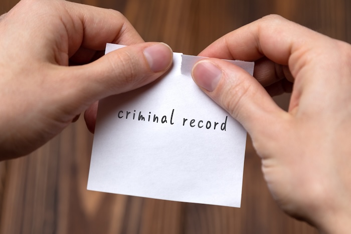 Hands tearing a paper labeled "criminal record" on a wooden surface.