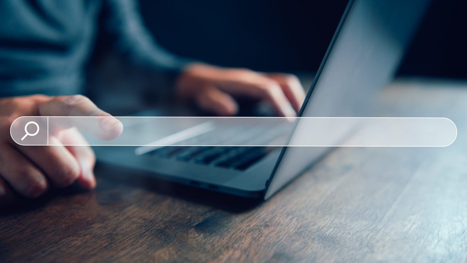 A person using a laptop, with one hand on the keyboard and the other about to click on a virtual search bar overlay displaying "USPhoneBook Opt Out." The background is blurred, focusing attention on the search action.