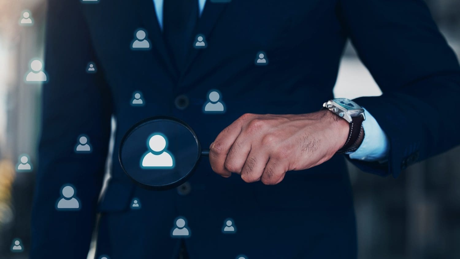 A person in a suit holding a magnifying glass, focusing on a digital icon of a human figure among various similar icons. The scene symbolizes the concept of searching, recruitment, or selection in a professional context, akin to using tools like ZoomInfo for precise candidate identification while respecting opt-out preferences.