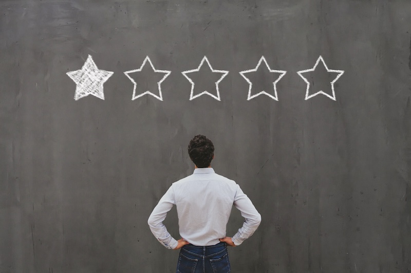 A person stands with hands on hips, facing a chalkboard with five stars drawn on it. Only the first star is filled in, while the remaining four stars are empty. The scene suggests evaluation or rating with a low score, highlighting the challenges of reputation management for lawyers.