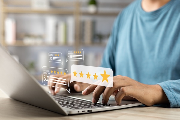 A person wearing a blue shirt types on a laptop keyboard. Floating graphics depict customer ratings with various star levels, including one 5-star rating prominently displayed. A high reputation score is evident among the visuals. Shelves in the background are softly blurred.