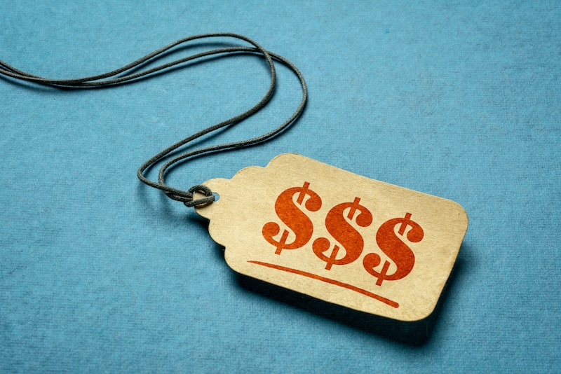 A brown price tag with three red dollar signs ($$$) printed on it hangs from a black string against a blue background.