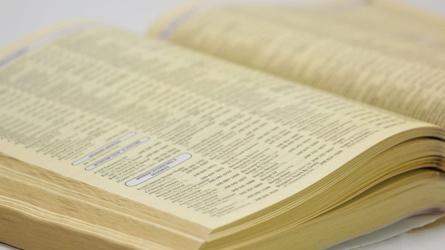 A close-up image of an open phone book. The yellowed pages capture various names, addresses, and phone numbers in many columns. Placed on a white surface, the text blurs towards the edges due to depth of field. This nostalgic scene reminds some why they choose to yellow pages opt out nowadays.